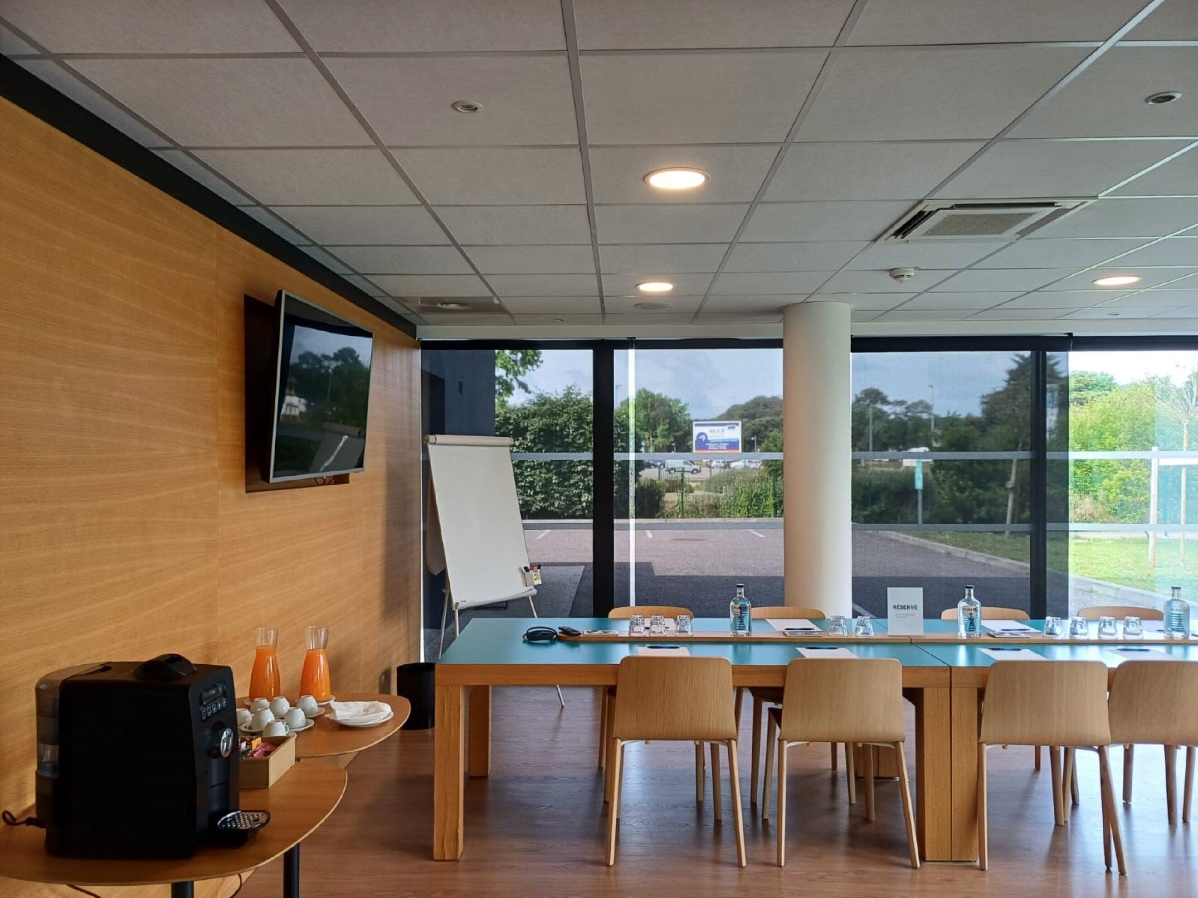 A conference room with a long table, chairs, a projector screen, and a view of the outside.