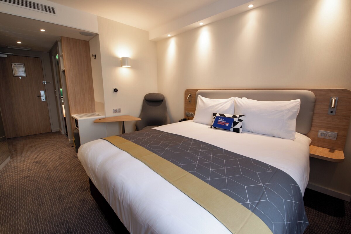 Hotellihuone, jossa on sänky, yöpöydät, tuoli ja työpöytä.