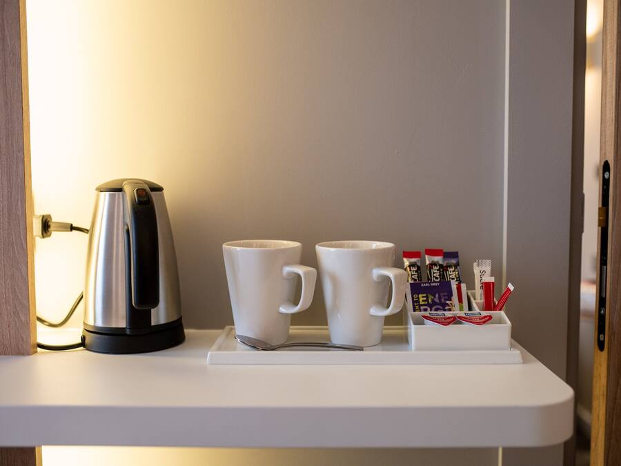 A white tray with a coffee maker and two white mugs on a white countertop.