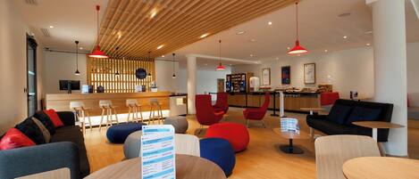 A modern lounge area with seating, tables, and a menu board.