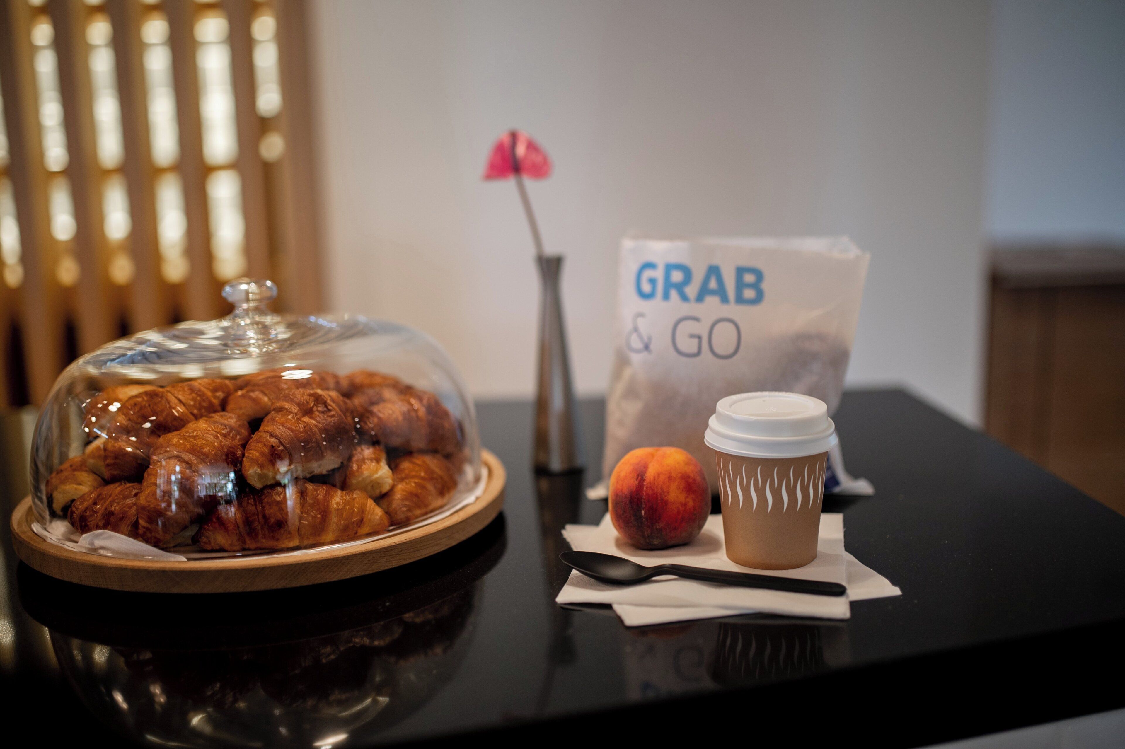 Una mesa con una vitrina de vidrio que exhibe comida, una taza de café, un melocotón y una bolsa 'GRAB & GO'.