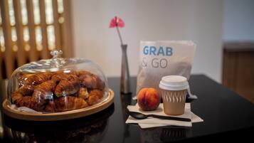 Une table avec une présentation de plats sous un dôme de verre, une tasse de café, une pêche et un sac « À EMPORTER ».