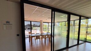 A modern meeting room with a large glass wall, wooden flooring, and a view of an outdoor parking area. - Holiday Inn Express Arcachon - La Teste by IHG (La Teste-de-Buch)