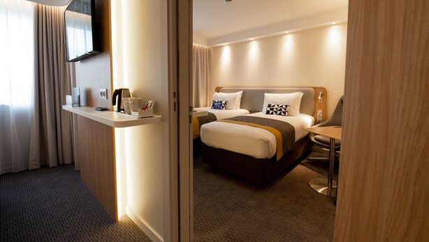 A hotel room with a bed, bedside tables, a TV mounted on the wall, and a window with curtains. - Holiday Inn Express Arcachon - La Teste by IHG (La Teste-de-Buch)