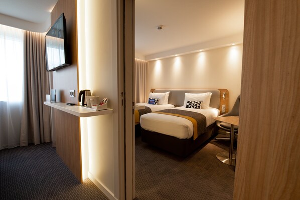 Een hotelkamer met een bed, nachtkastjes, een aan de muur bevestigde televisie en een raam met gordijnen.