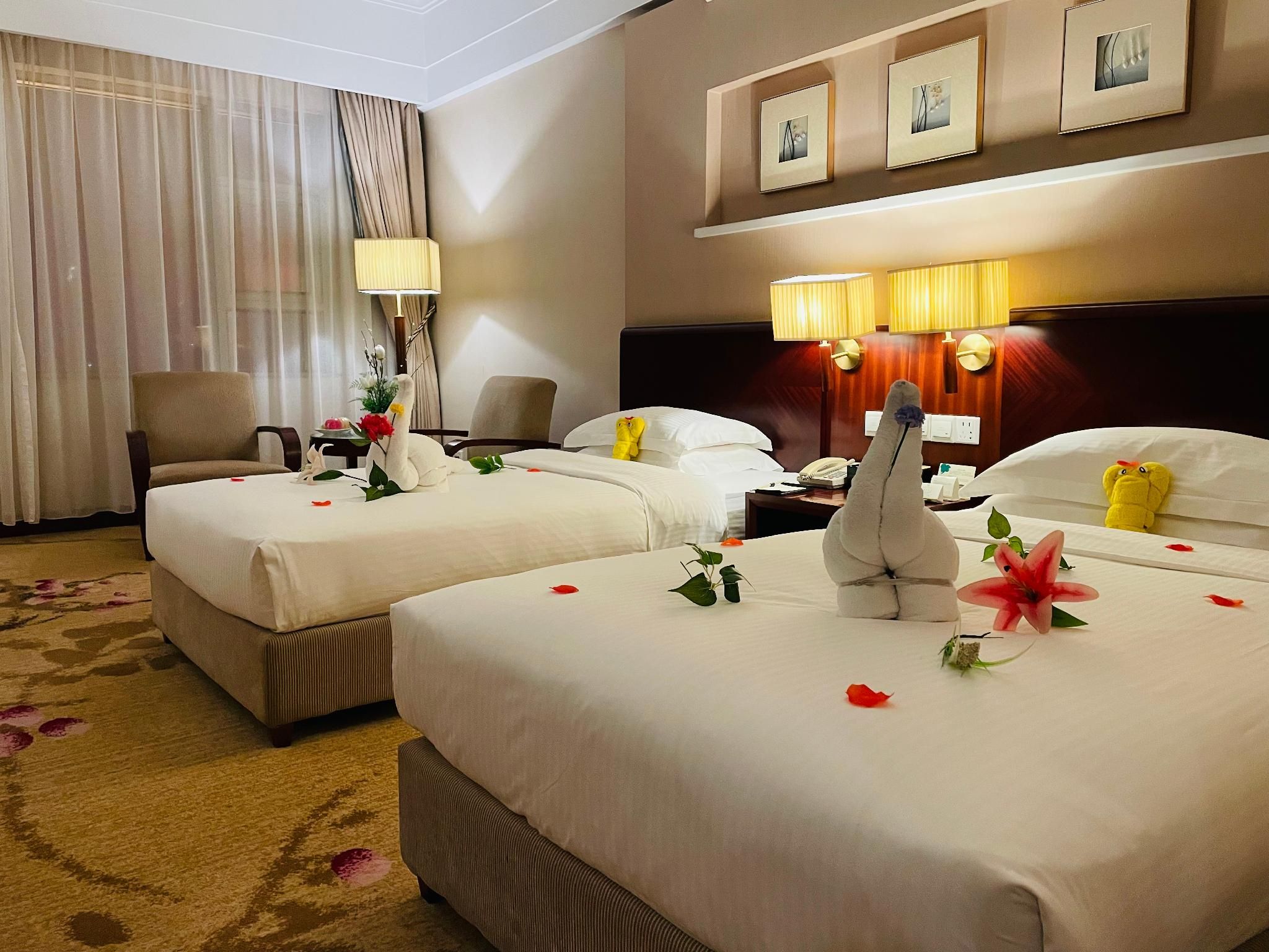 Ein Hotelzimmer mit zwei Betten, einem Schreibtisch, einem Stuhl, einer Lampe und einer Wand mit gerahmten Bildern.