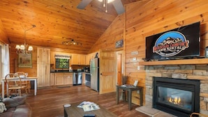 L’intérieur d’une cabane comprenant un coin repas, une cuisine et une cheminée.