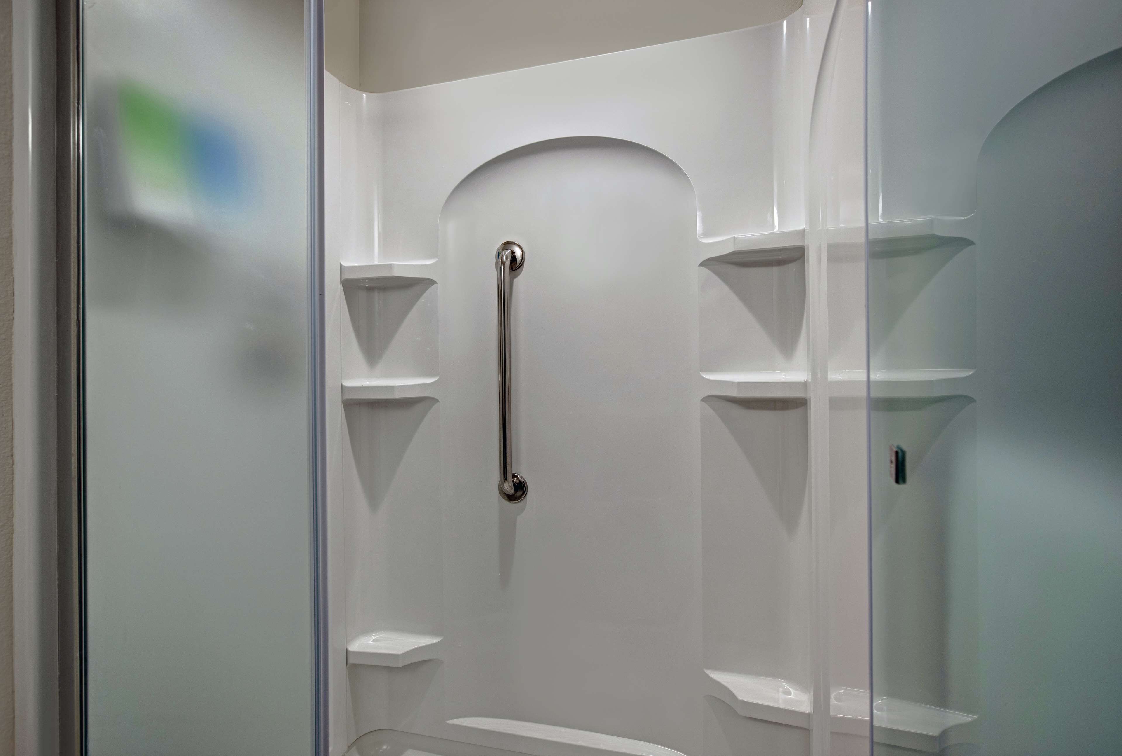 A modern bathroom with a glass shower enclosure, a handheld showerhead, and built-in shelves.