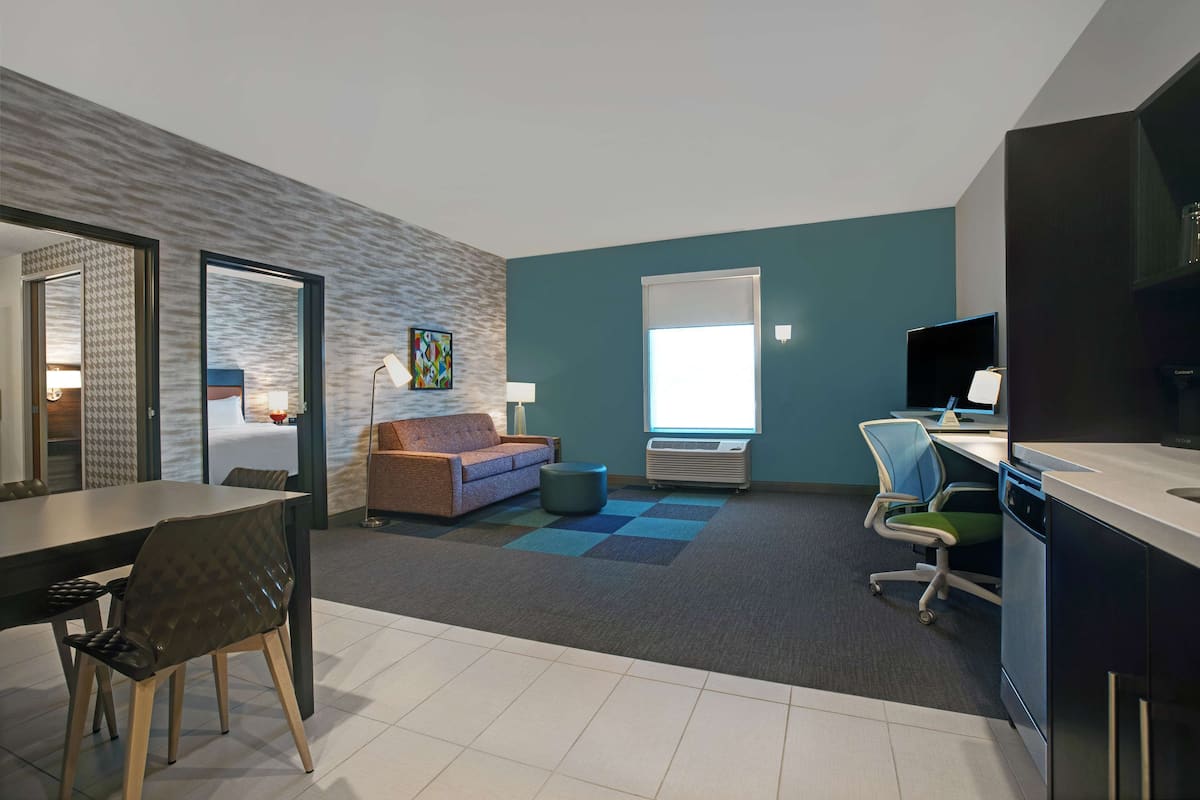 A modern hotel room with a dining area, a sofa, a desk, and a television.