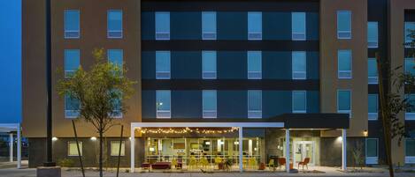 A modern building with multiple windows, a covered outdoor seating area, and a well-lit entrance.