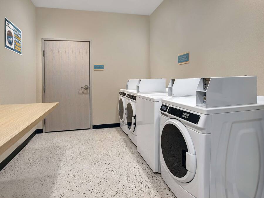 A laundry room with two washing machines, a dryer, and a wooden bench.