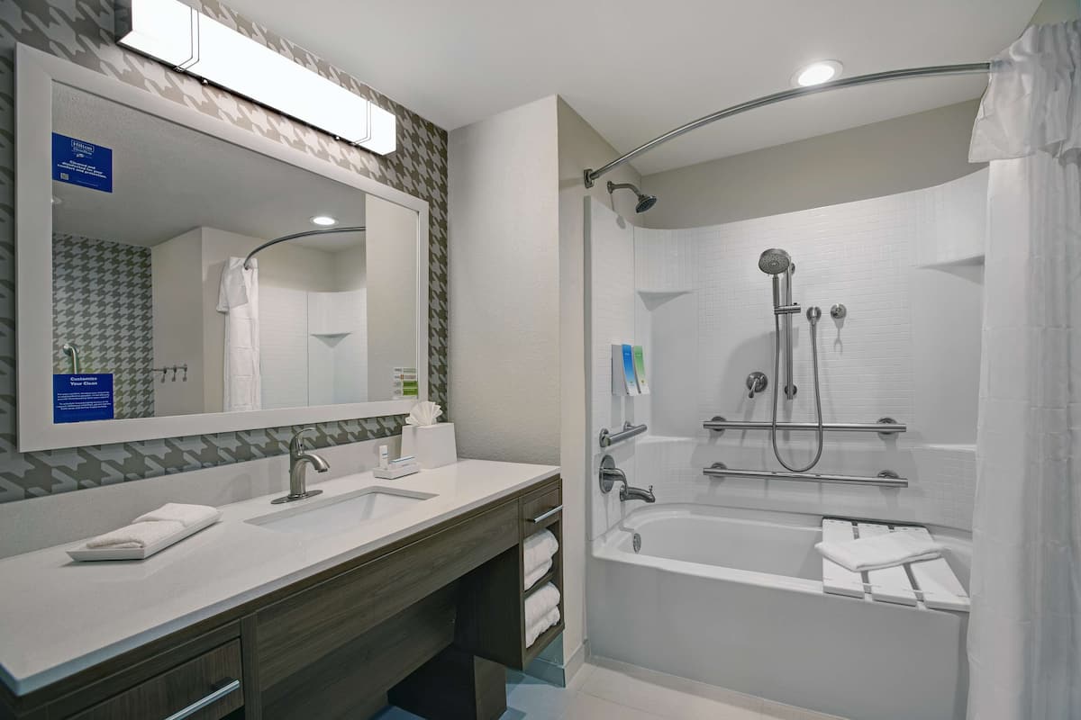 A modern bathroom with a large mirror, two sinks, a bathtub, and a shower.