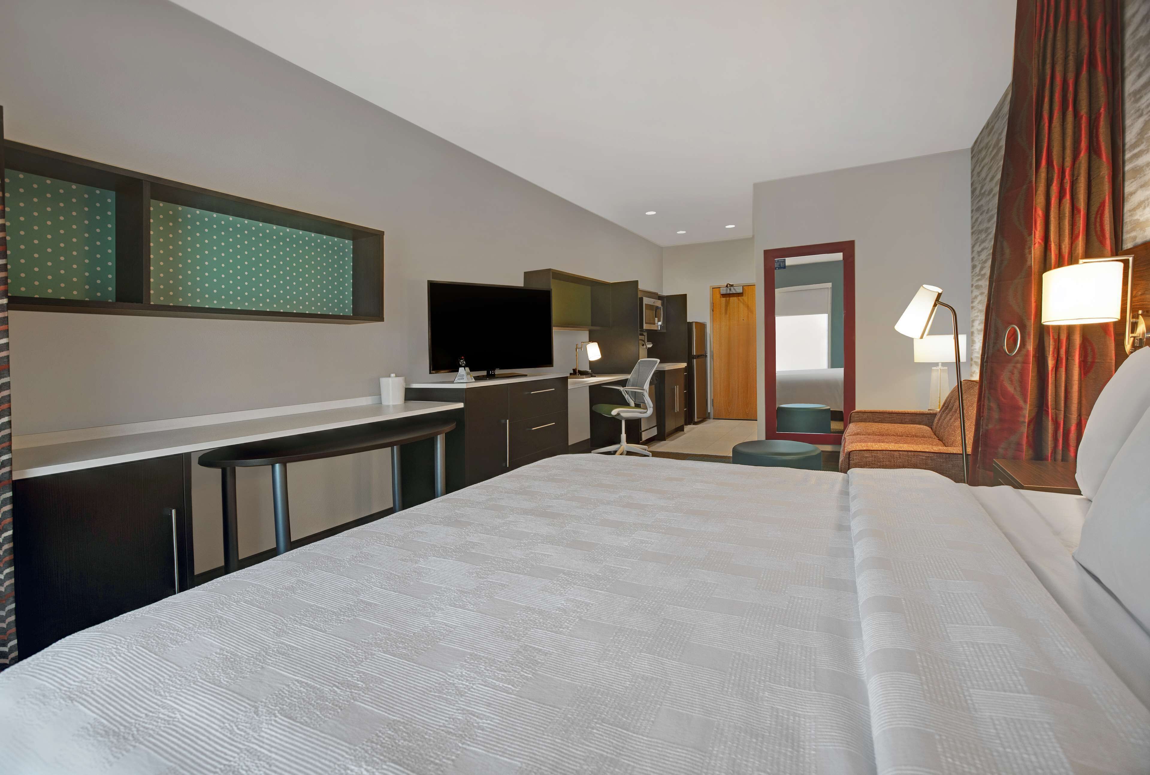 Une chambre d’hôtel avec un grand lit, un bureau avec un ordinateur, une télévision à écran plat, un miroir et une salle de bain avec des toilettes et un lavabo.