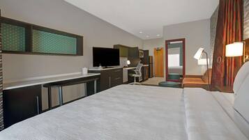 Une chambre d’hôtel avec un grand lit, un bureau avec un ordinateur, une télévision à écran plat, un miroir et une salle de bain avec des toilettes et un lavabo.