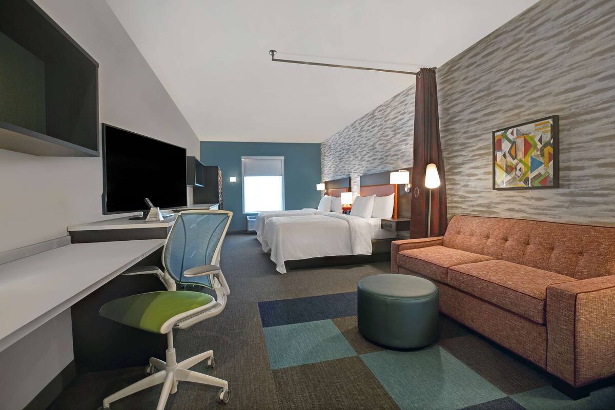 A hotel room with a desk, a bed, a sofa, a chair, a TV, and a painting on the wall.