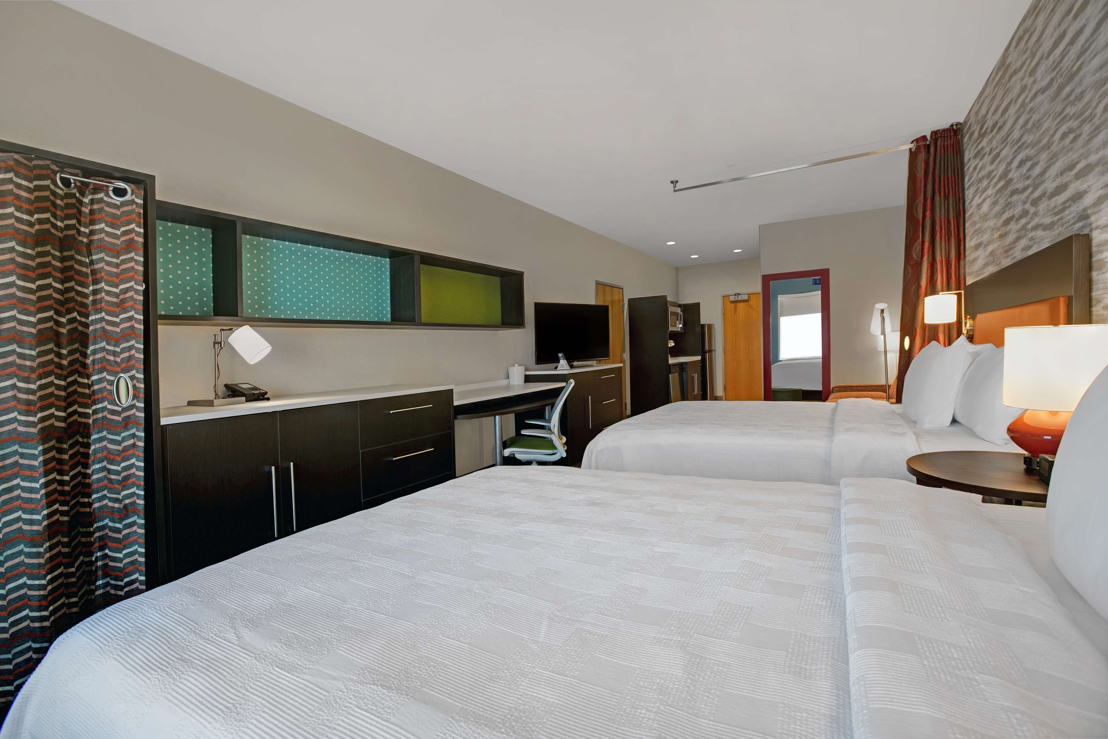 Habitación de hotel con dos camas, un escritorio, un televisor y un baño con cortina de ducha.