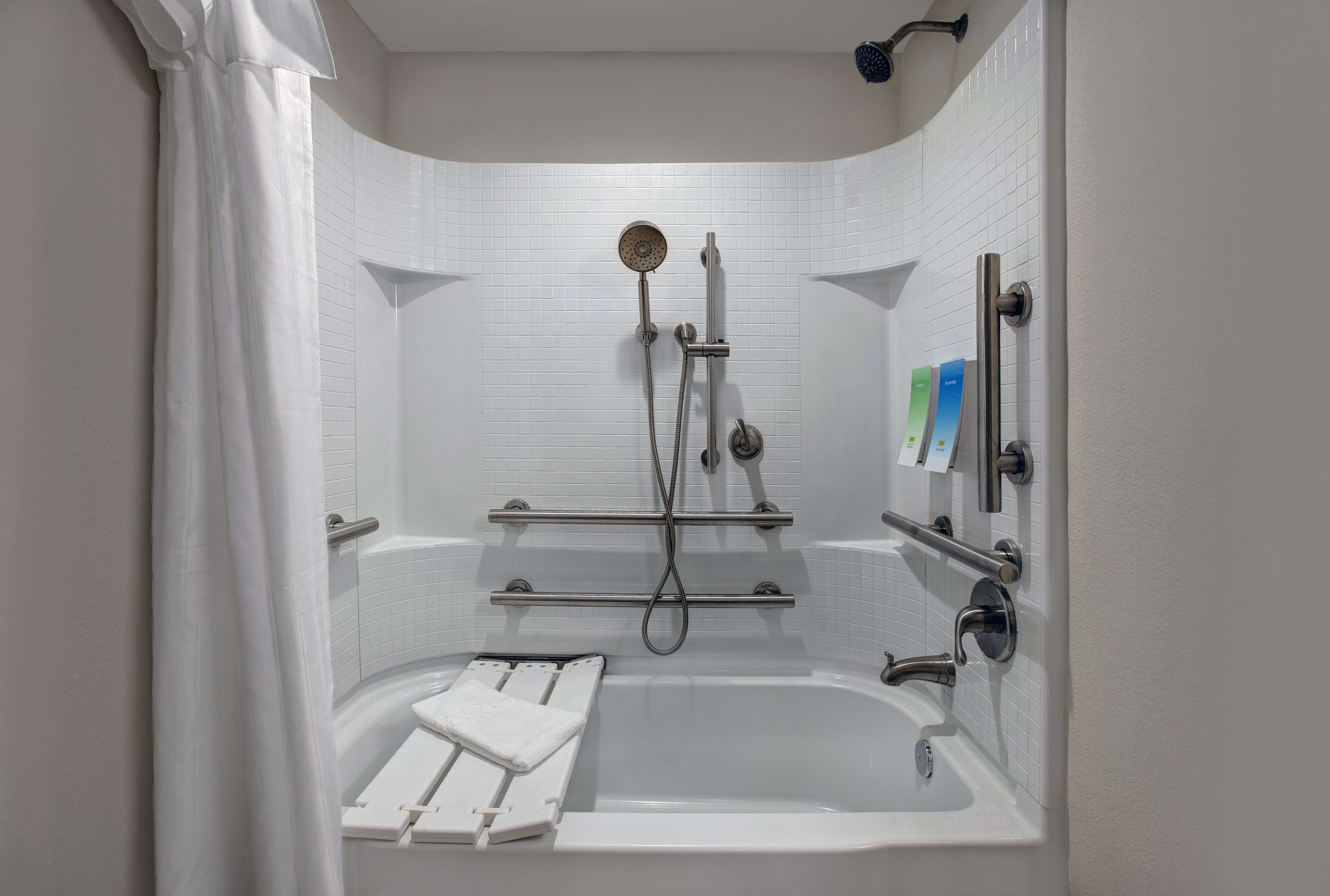 A modern bathroom with a walk-in shower, grab bars, and a white bathtub with a seat.