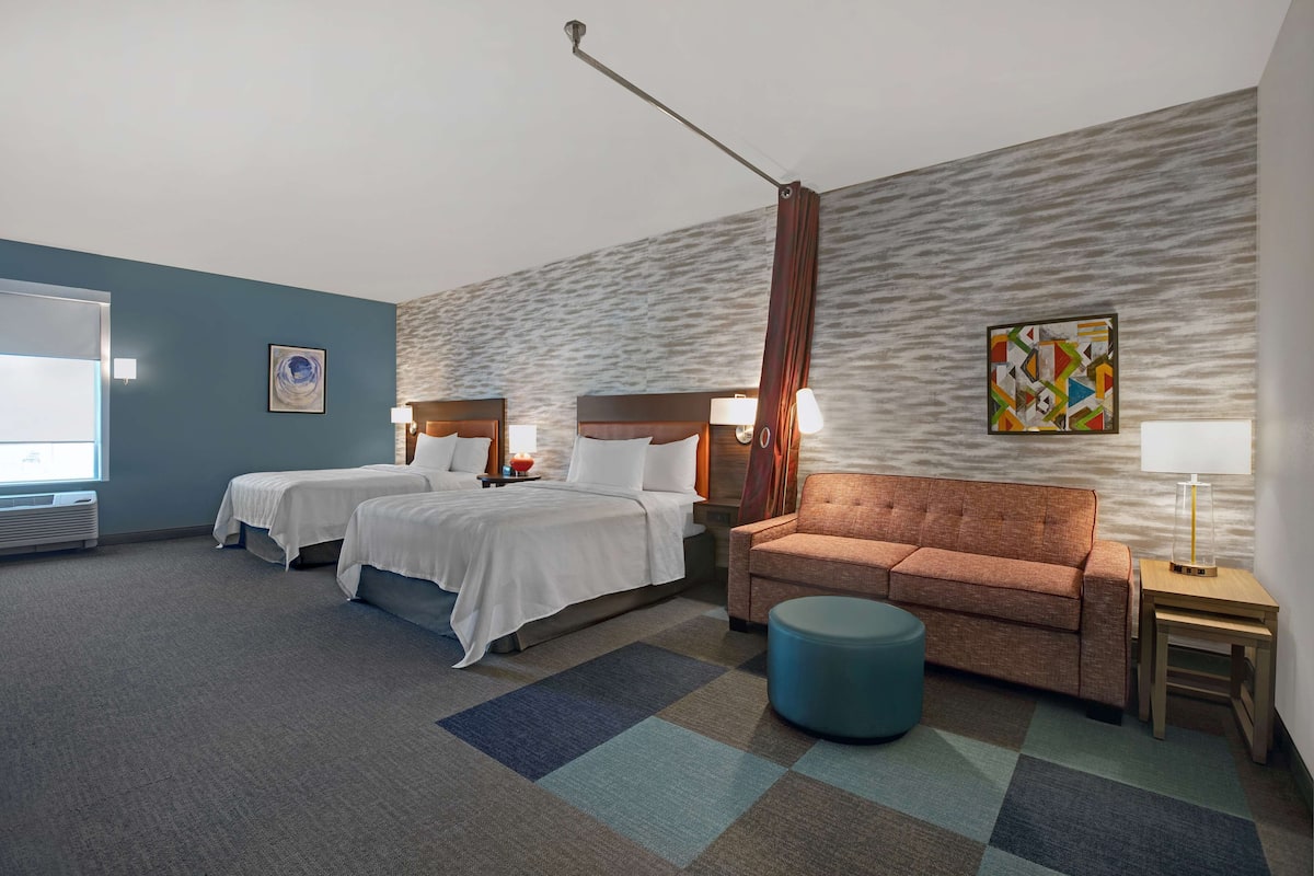 A hotel room with two beds, a sofa, a small table, and a lamp.