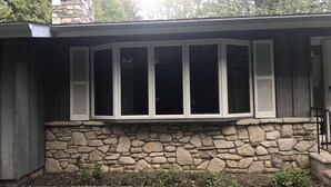 Una casa con cimientos de piedra, un ventanal con contraventanas y una chimenea.
