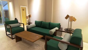 A modern living room with a green sofa set, a wooden coffee table, and two side tables with lamps. - Vinotel Cirebon (West Cirebon)