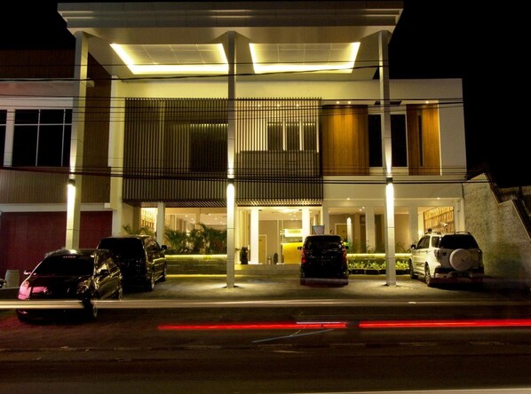 Ein moderner Hotelaufgang mit überdachter Auffahrt, mehreren parkenden Autos und einer gut beleuchteten Fassade.