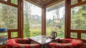 Habitación de esquina con una mesa, dos sillas, ventanas amplias y vistas al verdor exterior.