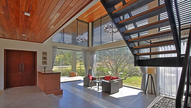 Un espacio habitable amplio con techo de madera, ventanas grandes, chimenea de ladrillo y una escalera.