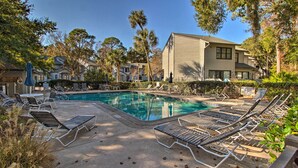 A swimming pool with lounge chairs, surrounded by trees and a building. - Walk to Forest Beach: Hilton Head Getaway! (Hilton Head Island)