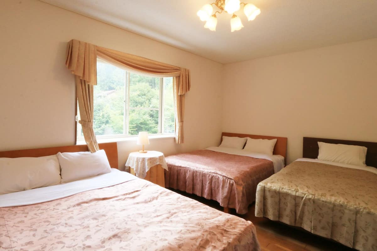 Ein Zimmer mit zwei Betten, einem kleinen Tisch und einem Fenster mit Vorhängen.