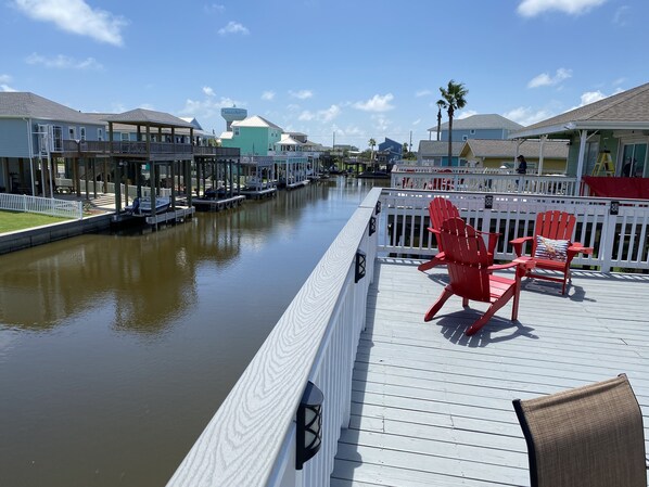 A waterfront deck with red Adirondack chairs and a white railing.