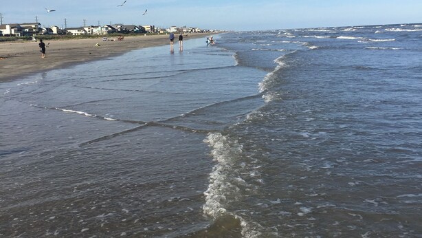 Una spiaggia con onde, cielo sereno e alcune persone.