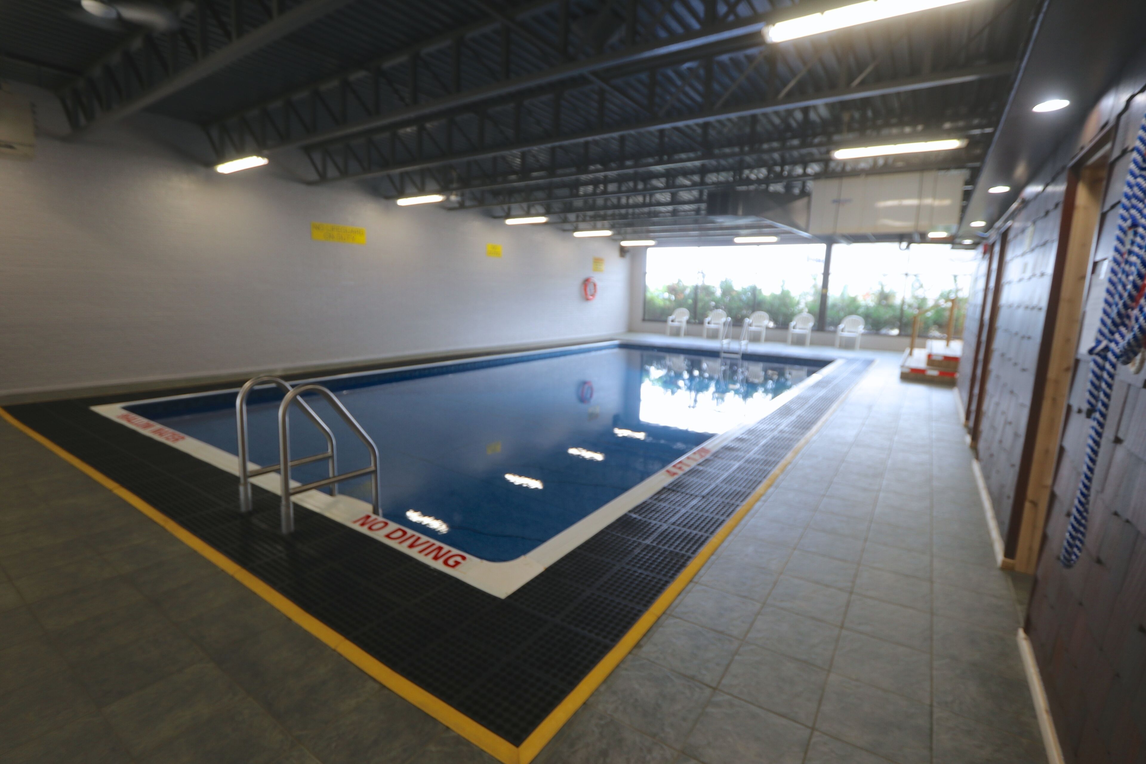 An indoor swimming pool with a diving board, tiled floor, and a clear pool area.