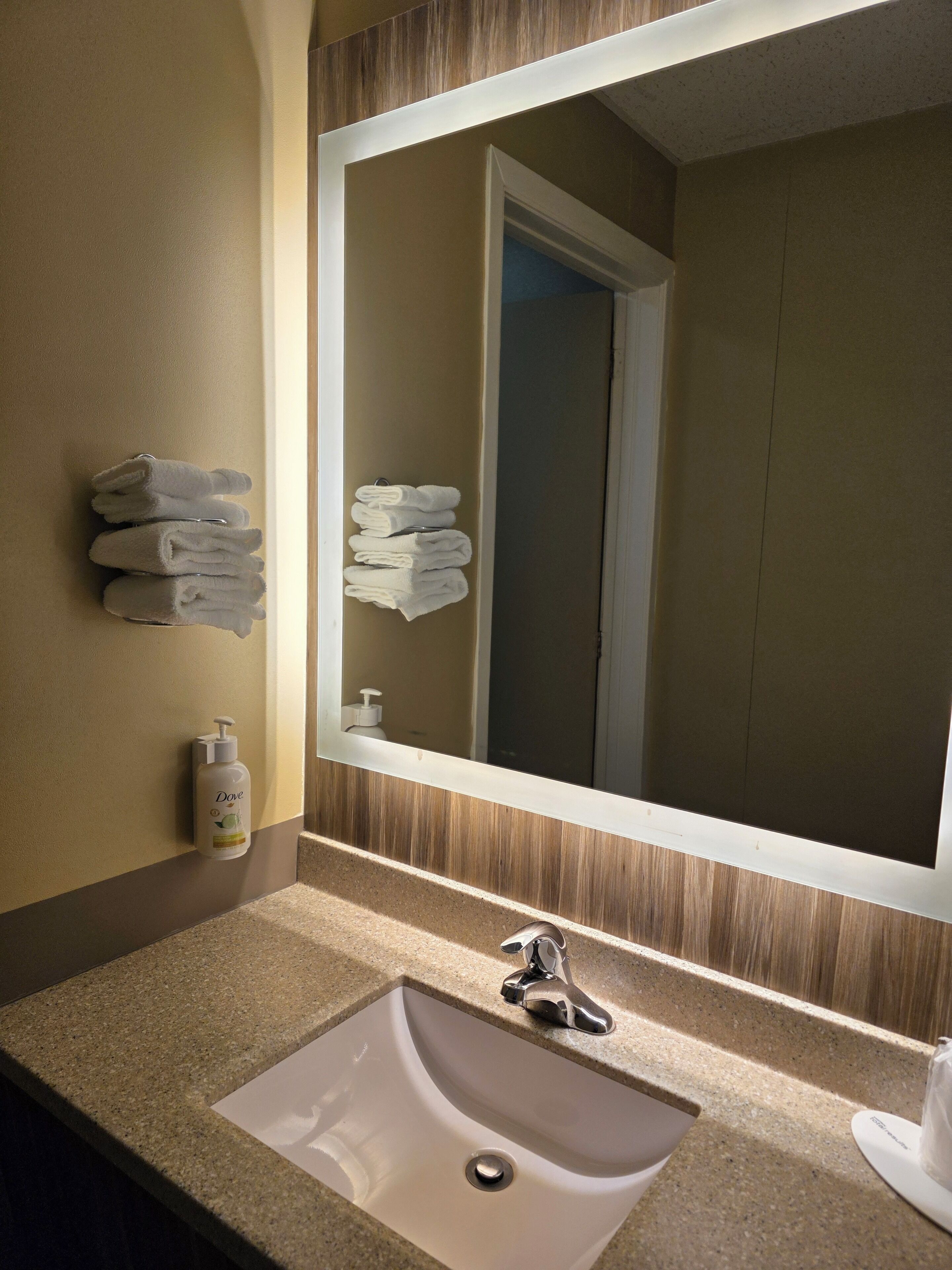 A bathroom with a sink, mirror, towels, and toiletries.