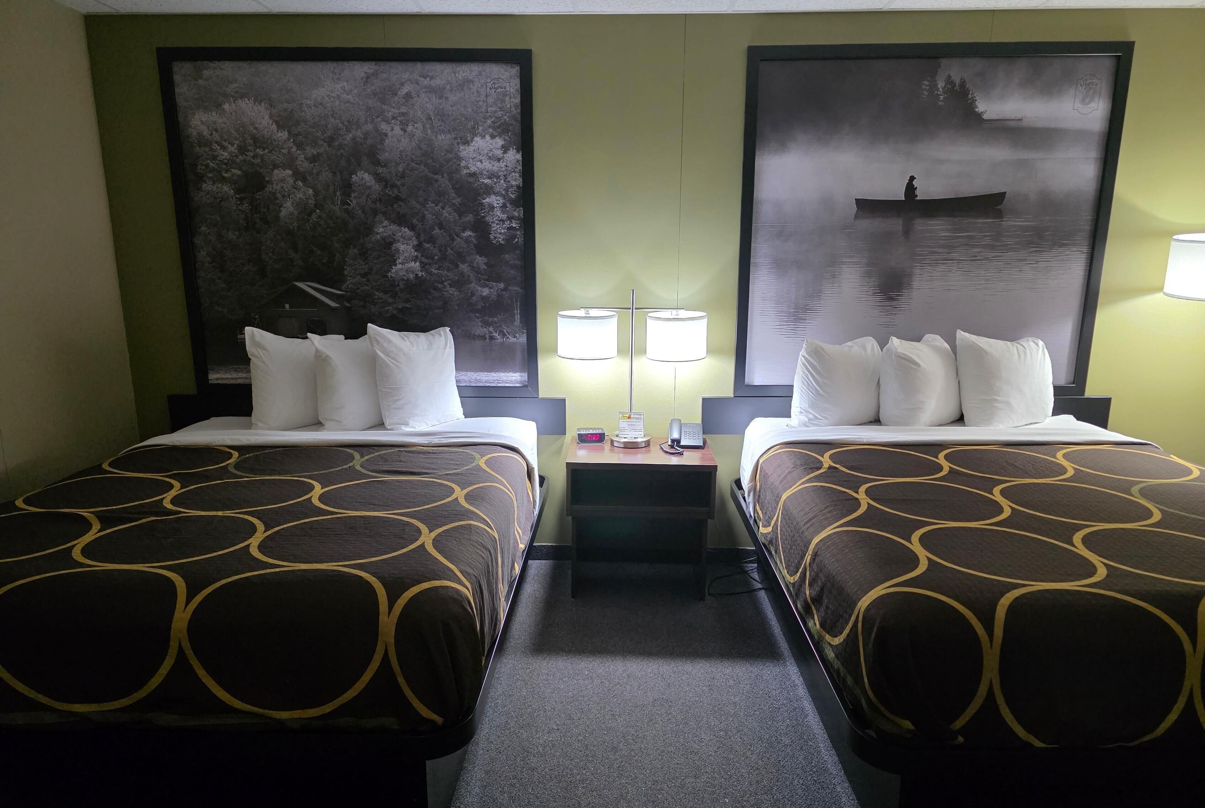 Une chambre d’hôtel avec deux lits, chacun recouvert d’une couvre-lit à motifs, une table de chevet avec une lampe et deux grandes images encadrées accrochées aux murs.