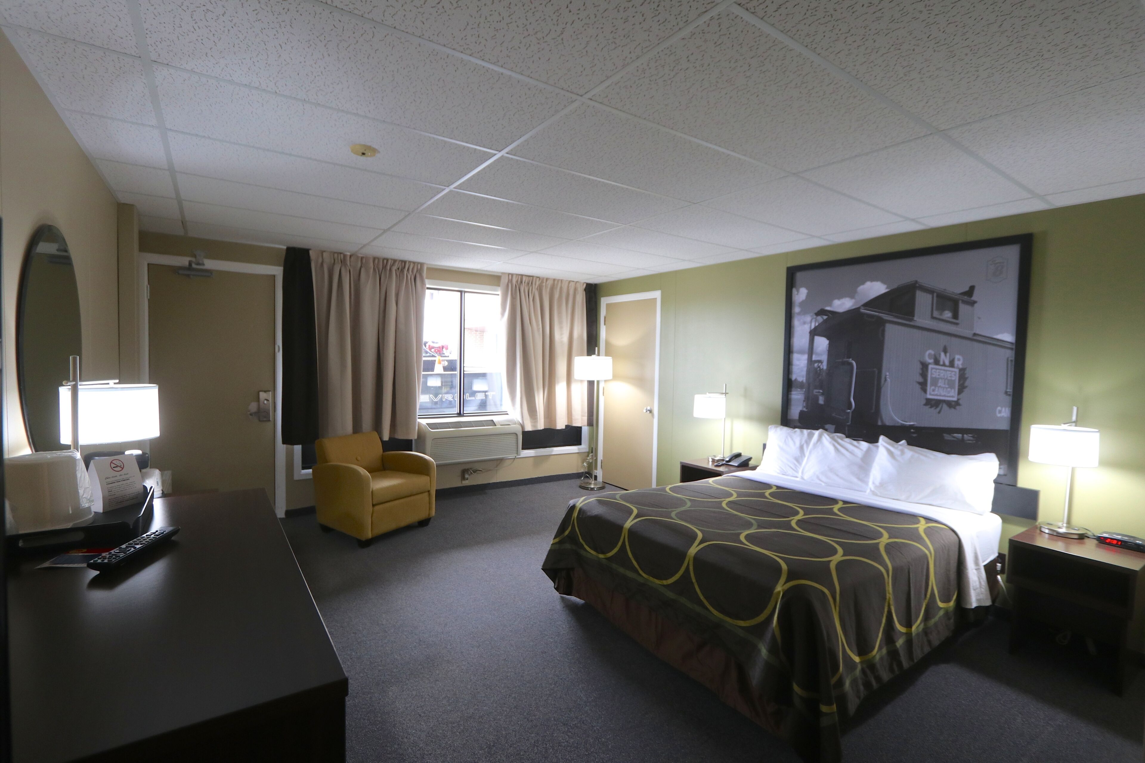 Una habitación de hotel con cama, escritorio, silla, televisor y ventana con cortinas.
