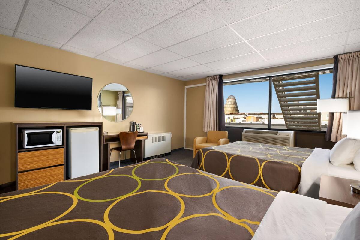Hotelkamer met twee bedden, een bureau, een televisie, een magnetron en uitzicht op een stadslandschap.