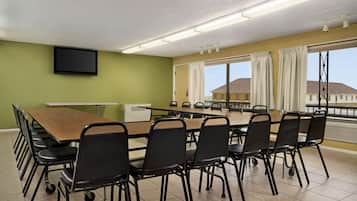 Un salón de conferencias con una larga mesa y sillas, un televisor de pantalla plana en la pared y amplias ventanas con cortinas.
