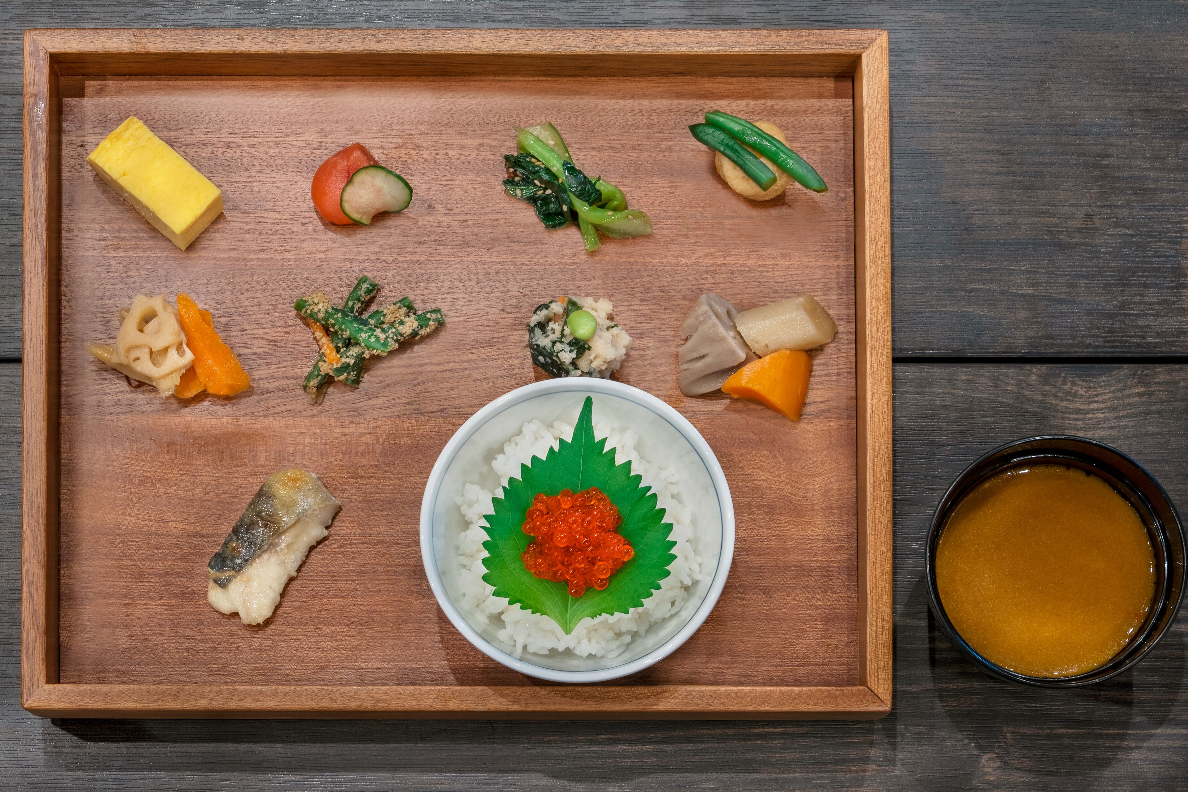Un plateau en bois contenant divers plats japonais, notamment des sushis, des sashimis et des légumes marinés.