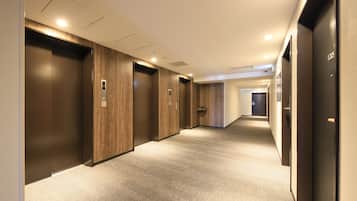 A modern hallway with wooden paneling, carpeted floors, and a series of elevators.