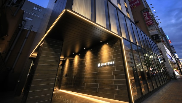 Un edificio moderno con fachada de vidrio y señalización iluminada que dice "QUINTESSA".