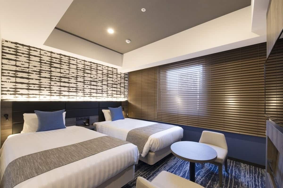 Ett hotellrum med två sängar, ett litet runt bord, en stol, en tv och en vägg med ett mönster.