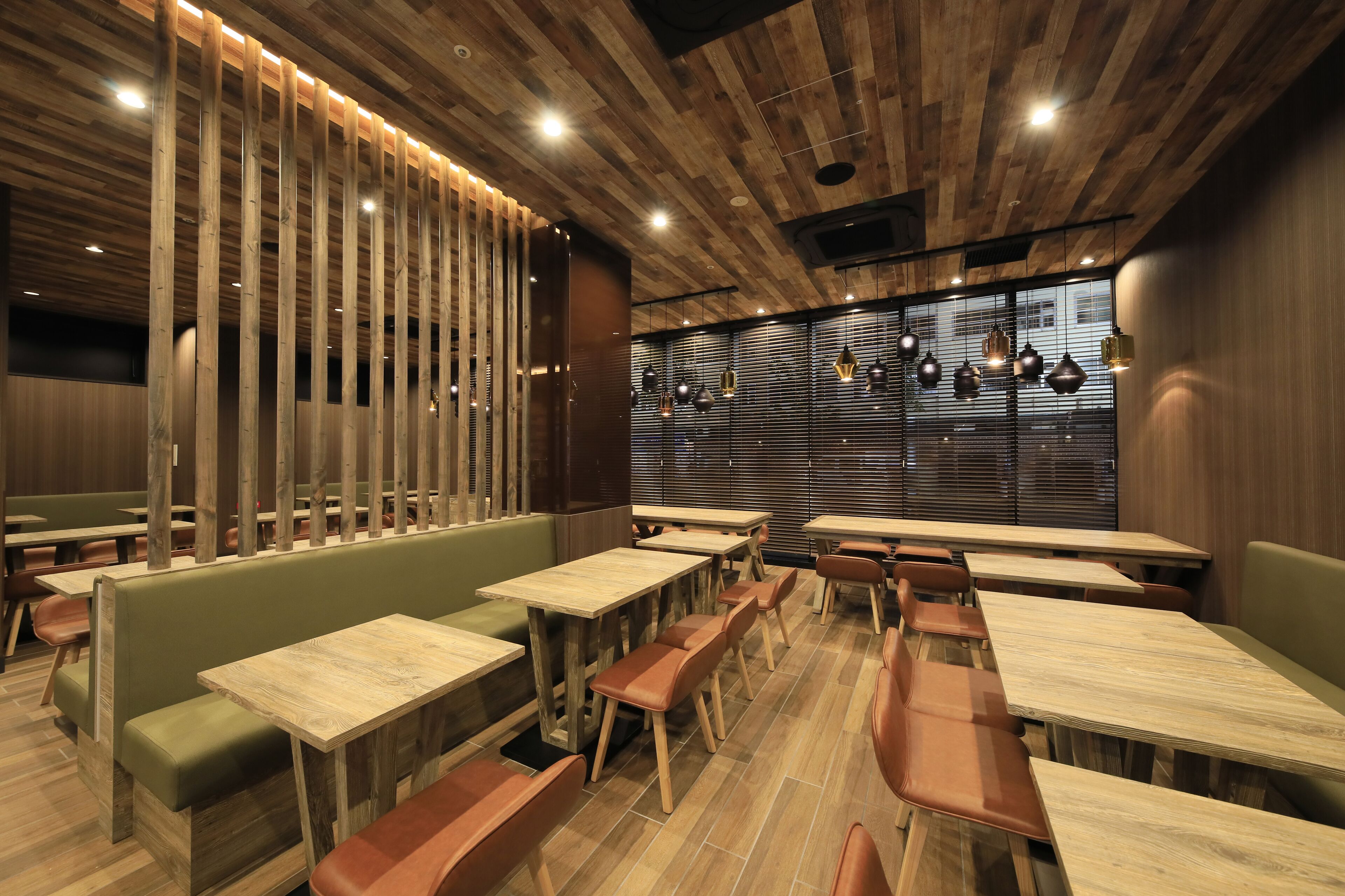 A restaurant with wooden tables and green cushioned booths, featuring a modern interior with wooden ceiling panels and pendant lighting.