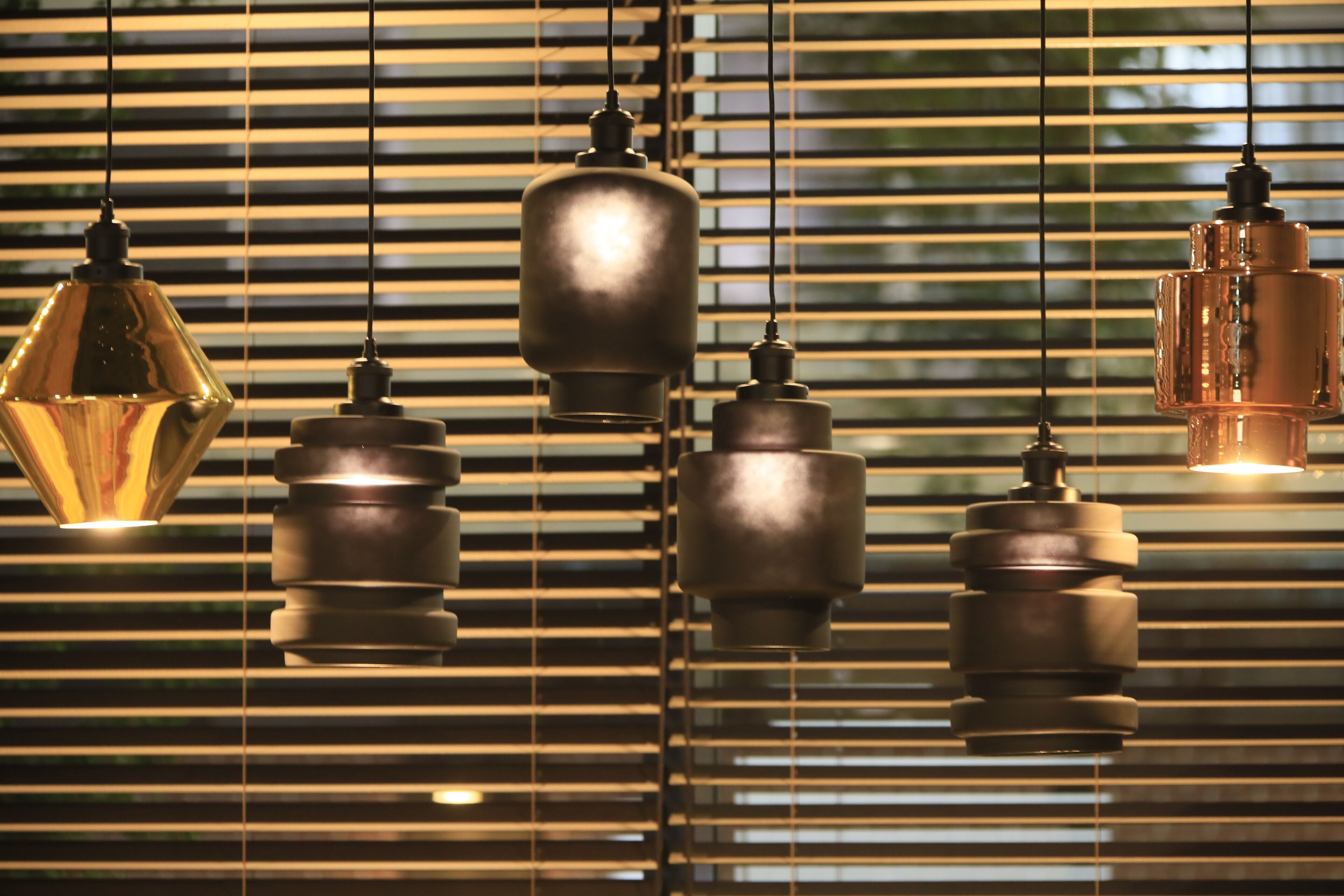 A series of hanging pendant lights with a reflective surface, suspended against a background with horizontal blinds.