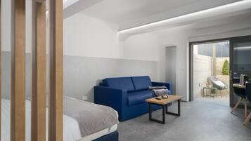 A modern hotel room with a bed, a blue sofa, a small table, and a desk with a chair.