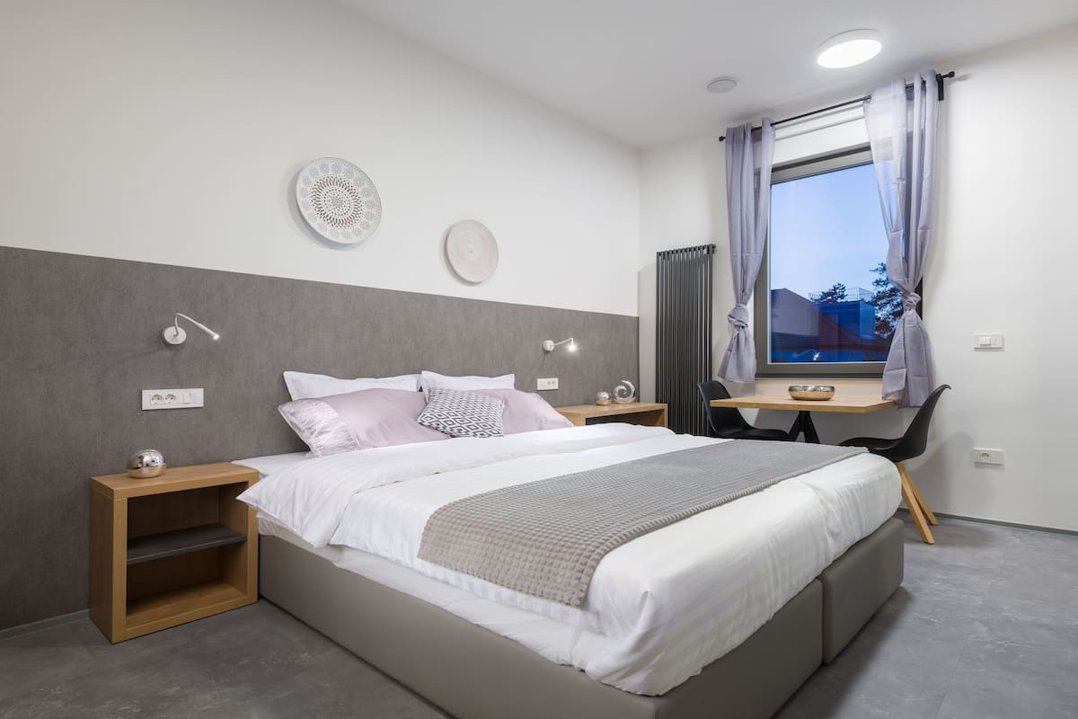 Een moderne slaapkamer met een groot bed, nachtkastjes, een bureau en een raam met gordijnen.
