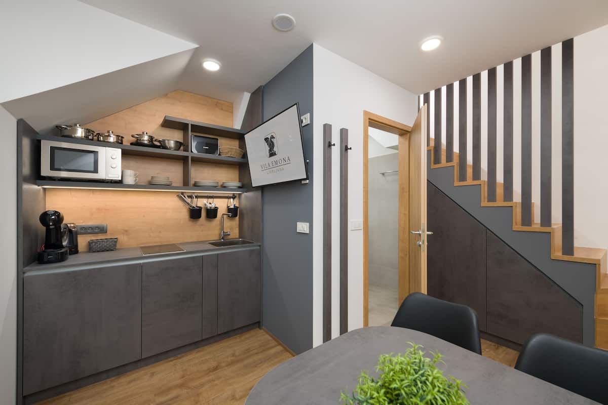 Een moderne keuken met grijze kastjes, een magnetron en een koffieapparaat. Daarboven hangt een houten plank boven de spoelbak en aan de muur een ingelijste foto.