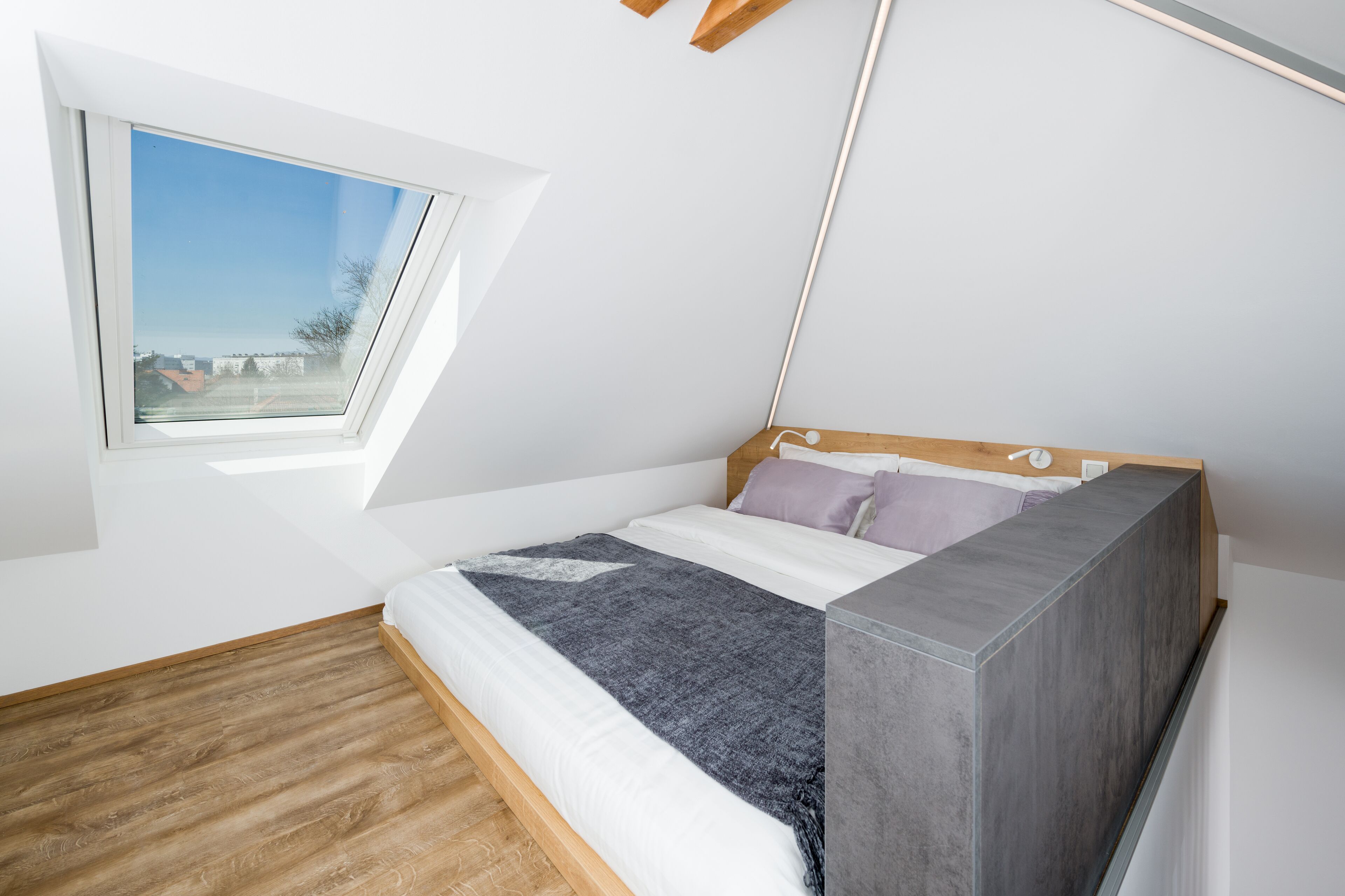 Un dormitorio con tragaluces, una cama con cabecera gris y suelo de madera.