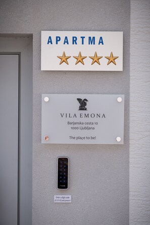 Un panneau mural indiquant « APARTMA » et affichant quatre étoiles, une plaque portant l’inscription « VILA EMONA » et l’adresse, et un clavier avec des instructions.