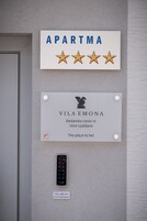 Placa na parede com 'APARTMA' e quatro estrelas, uma placa com 'VILA EMONA' e endereço, e um teclado com instruções.