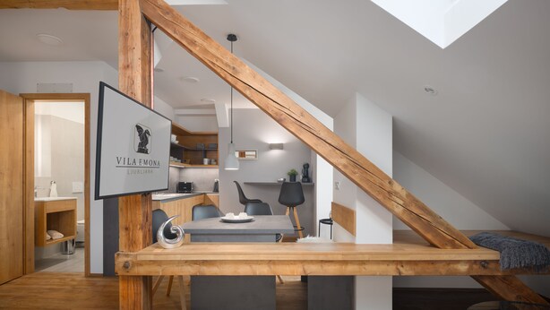 Een modern loft met zichtbare houten balken, een eethoek met tafel en stoelen, een keuken op de achtergrond en een dakraam erboven.
